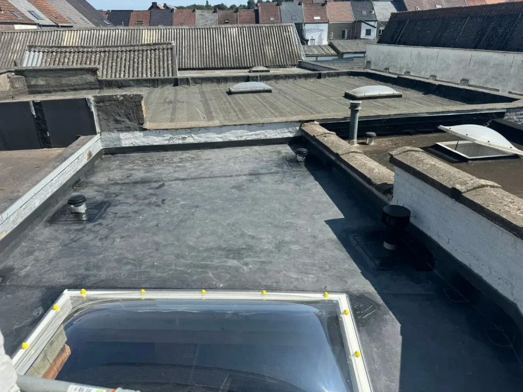 Plat dak met EPDM-dakbedekking en waterdicht ingewerkte dakdoorvoeren voor ventilatie, met een lichtkoepel op de voorgrond