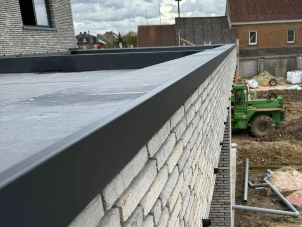 Strak afgewerkte dakrand van een plat dak met antraciete aluminium daktrim boven een gevel in lichte baksteen
