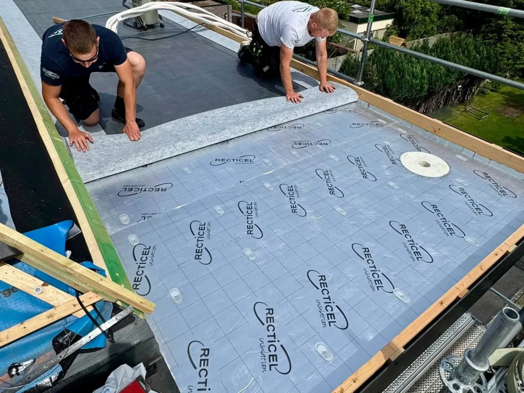 Dakwerkers plaatsen PIR-isolatieplaten op een plat dak, over het dampscherm